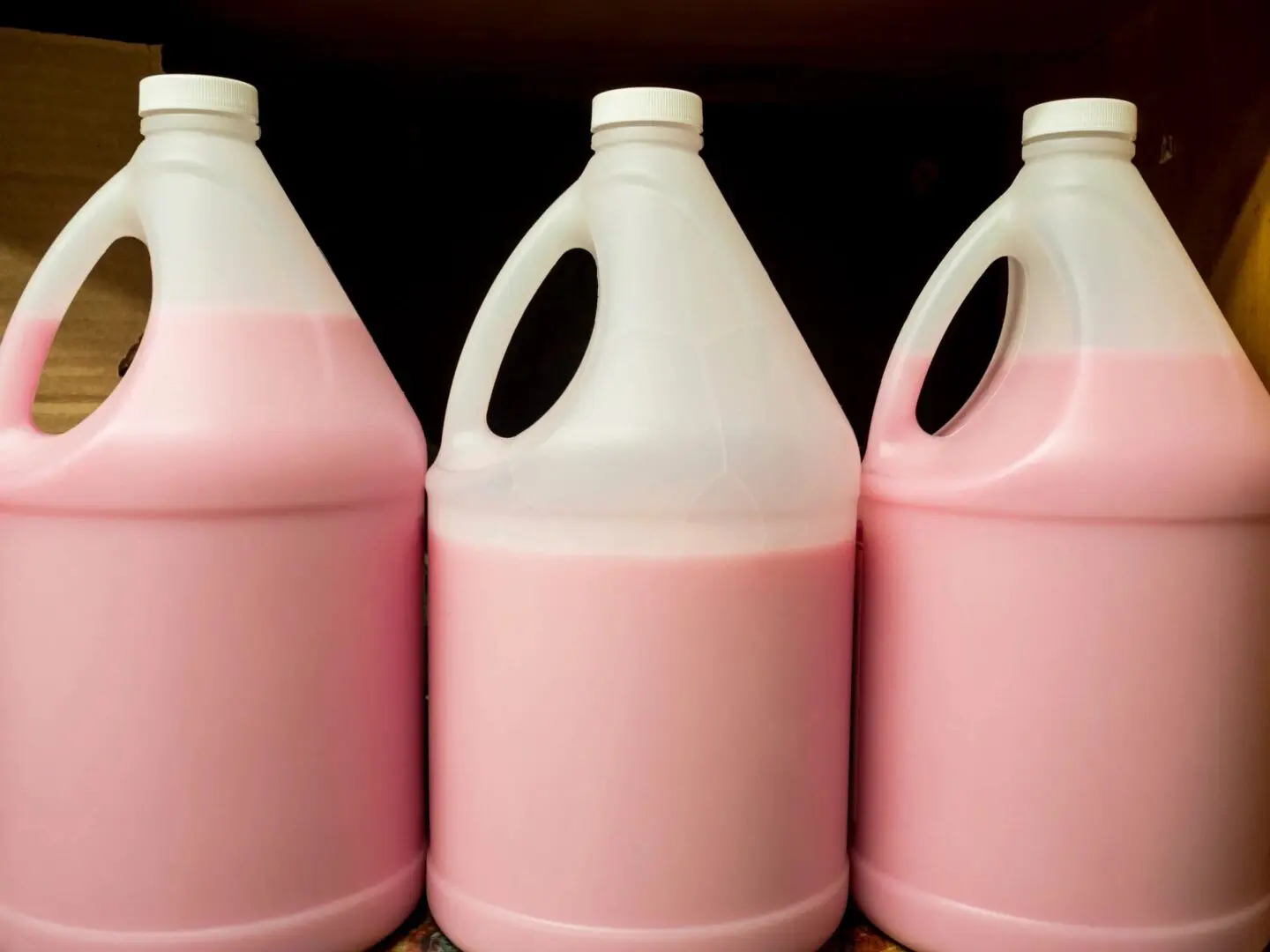 Three pink plastic jugs of soap sitting on a shelf.